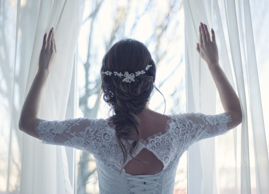 A woman dressed in white looks out the curtains dreaming of the future story of her life.